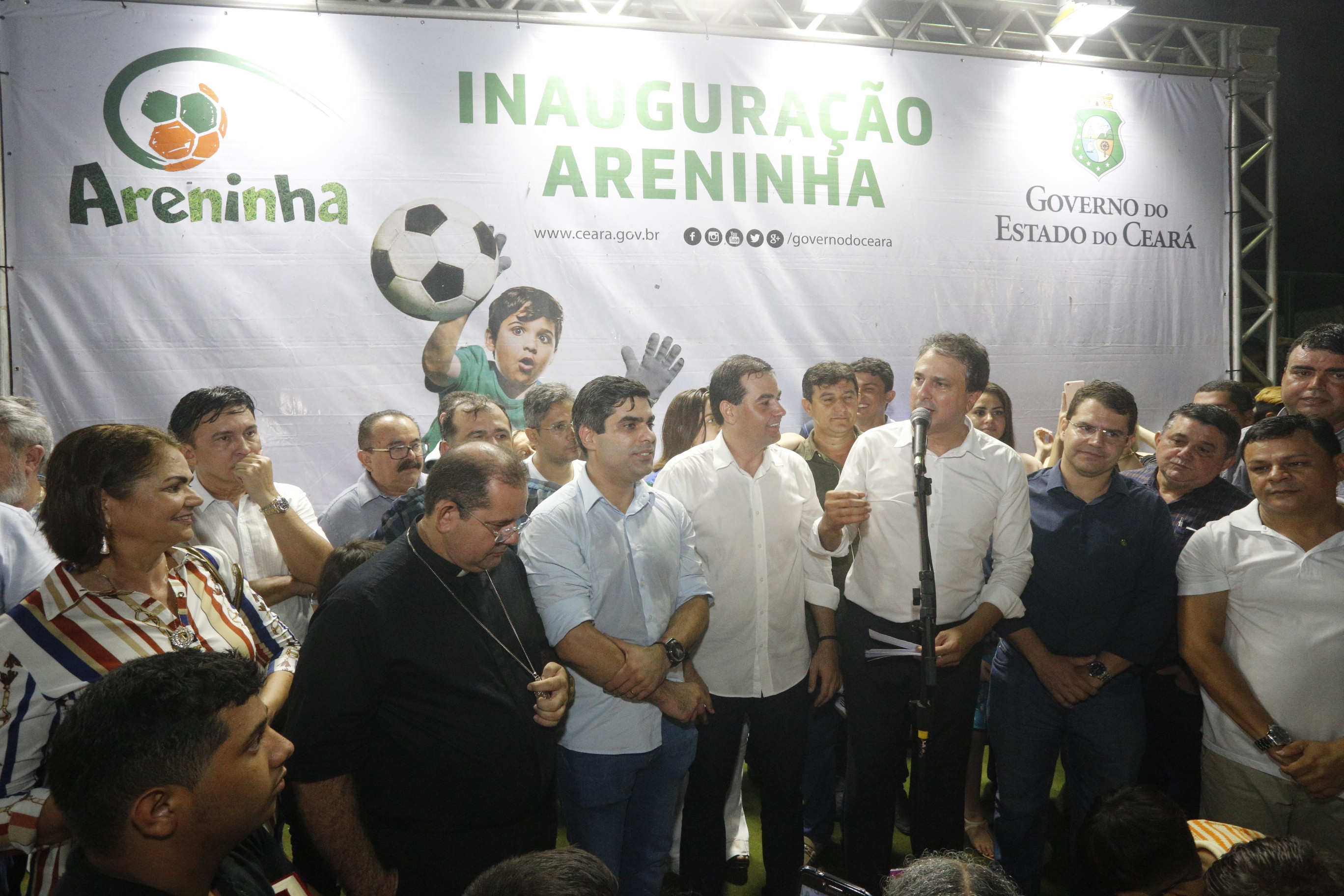 Governador anuncia outros benefícios para população de Umirim, no palco do evento, diante da placa que registra a inauguração da Areninha, acompanhado da população e autoridades locais