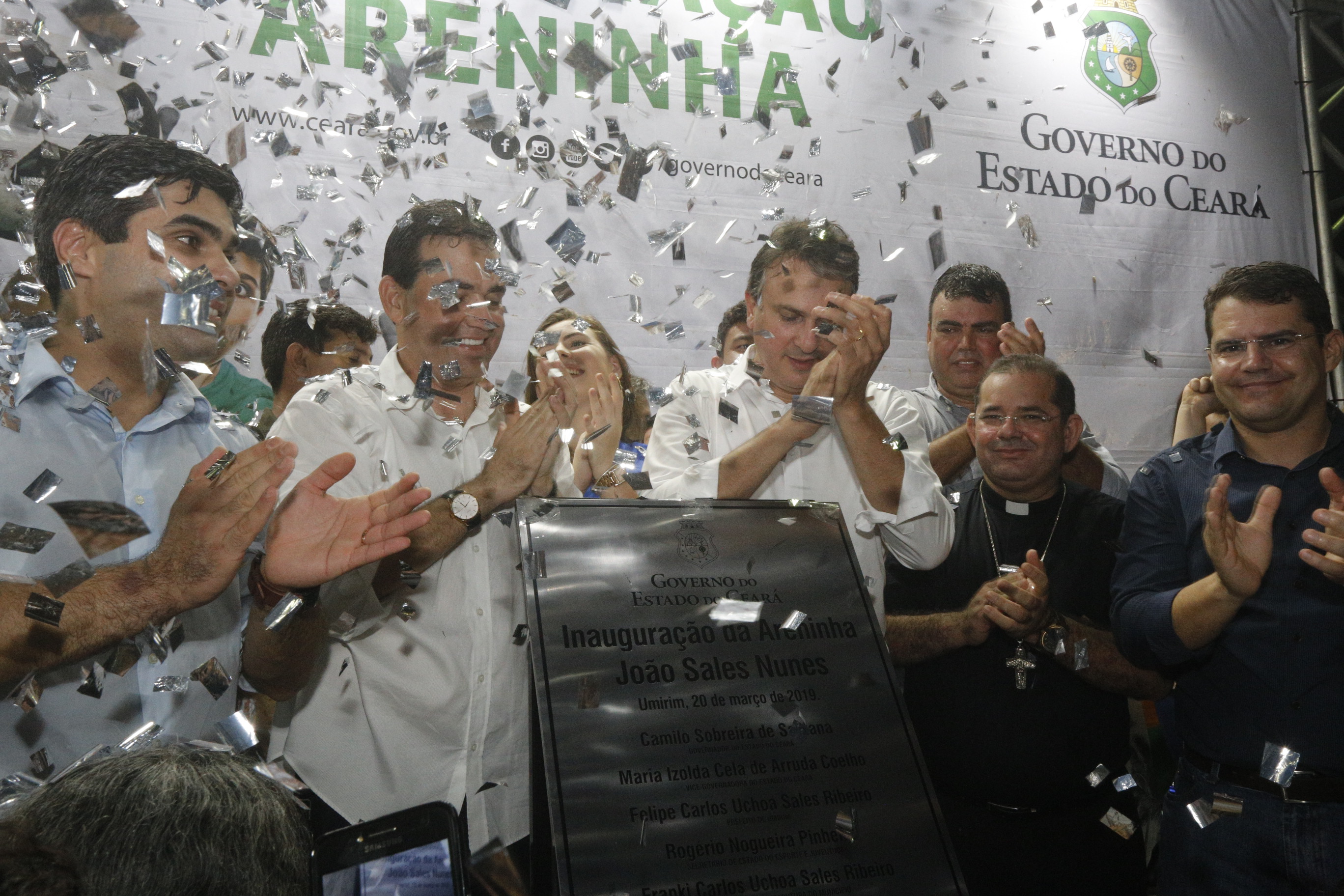 Governador do Ceará bate palmas junto ao povo de Umirim que celebra a inauguração da Areninha diante da placa que registra o momento